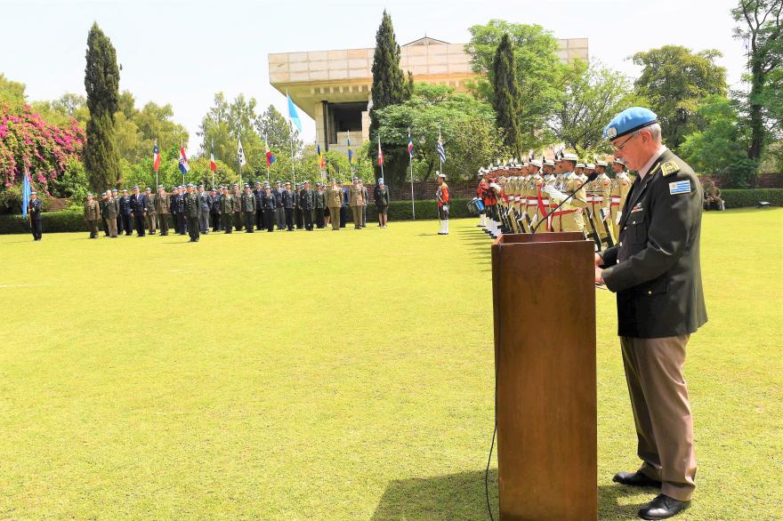 UN officer in uniform speaks at a podium outdoors during a formal ceremony, with soldiers standing in formation on a lawn.